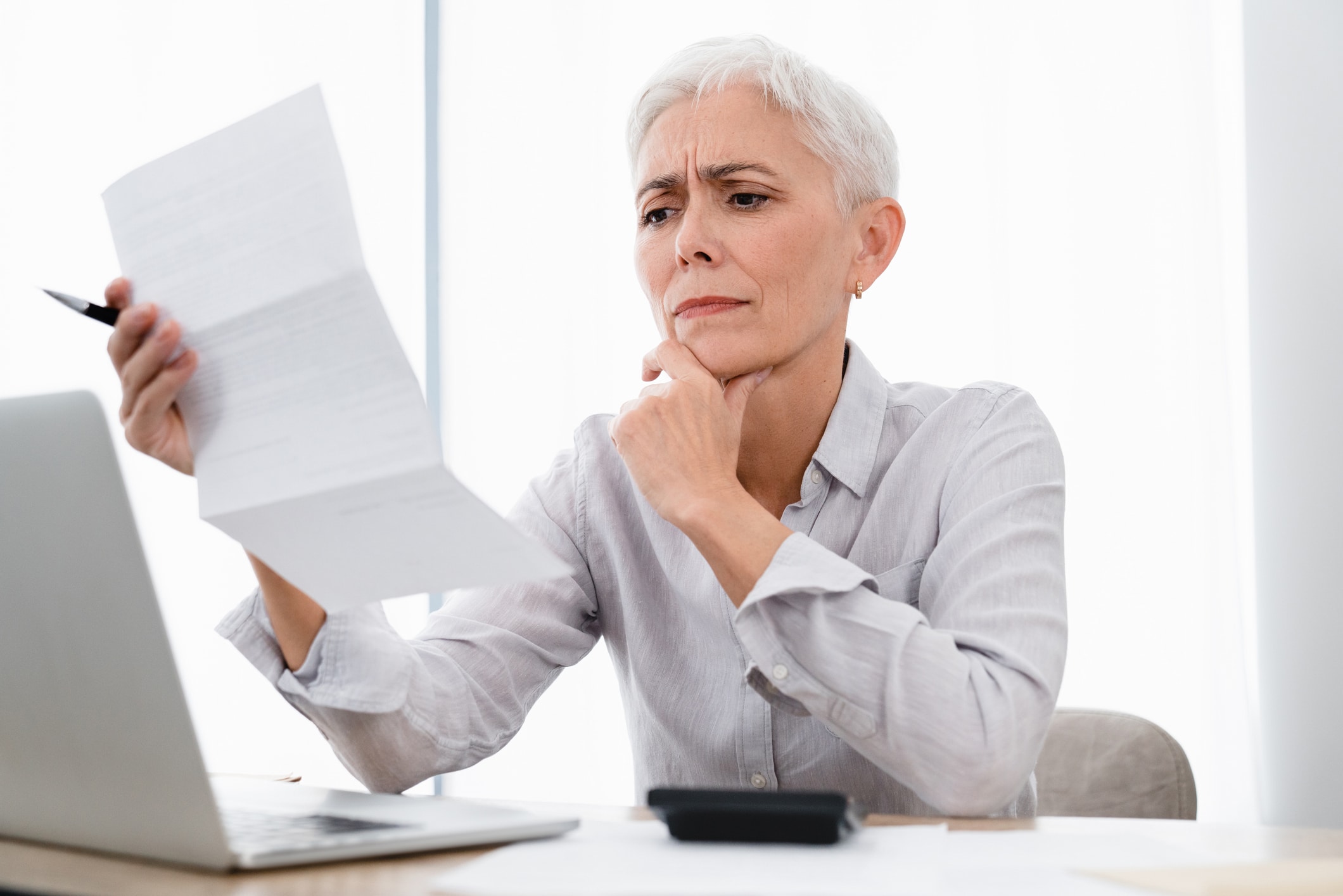 confused caucasian mature businesswoman paying bills using laptop at office.