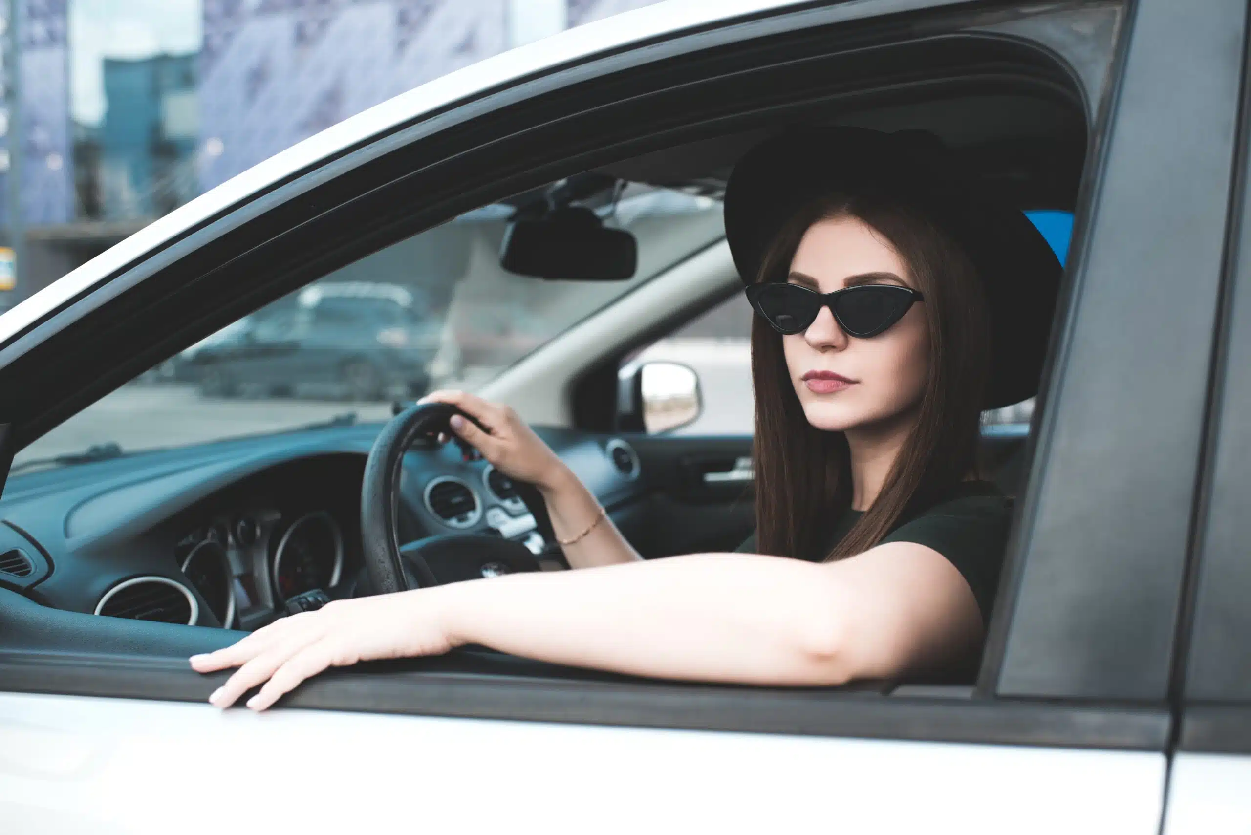 stylish girl 20 24 year old driving car outdoors. looking at camera.
